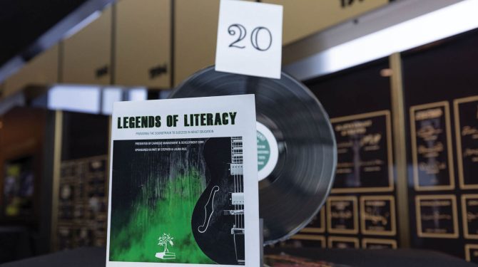 Program with guitar on the cover propped up against a vertical vinyl record with plaques in the background